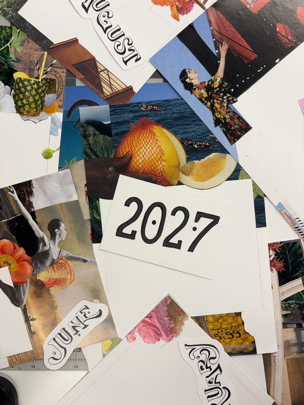 A collage of printed cards and photos scattered on a surface, including monthly labels like August, June, a large '2027' card, fruit imagery, a pineapple, and fashion/lifestyle photos.